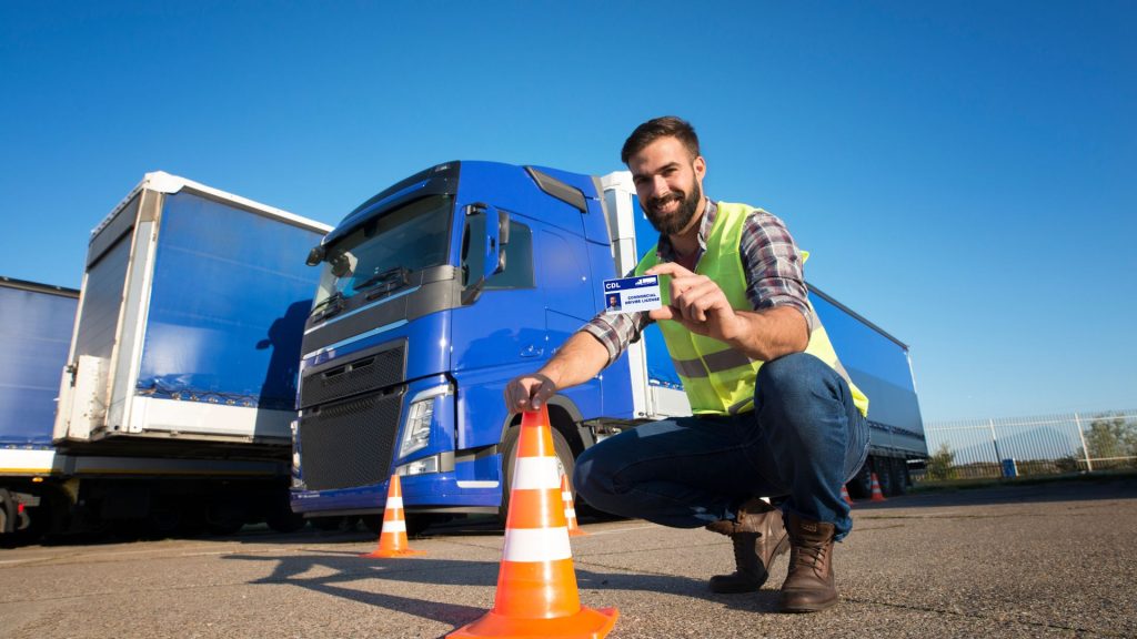 Man kneeling and touching a construction cone while holding a CDL.